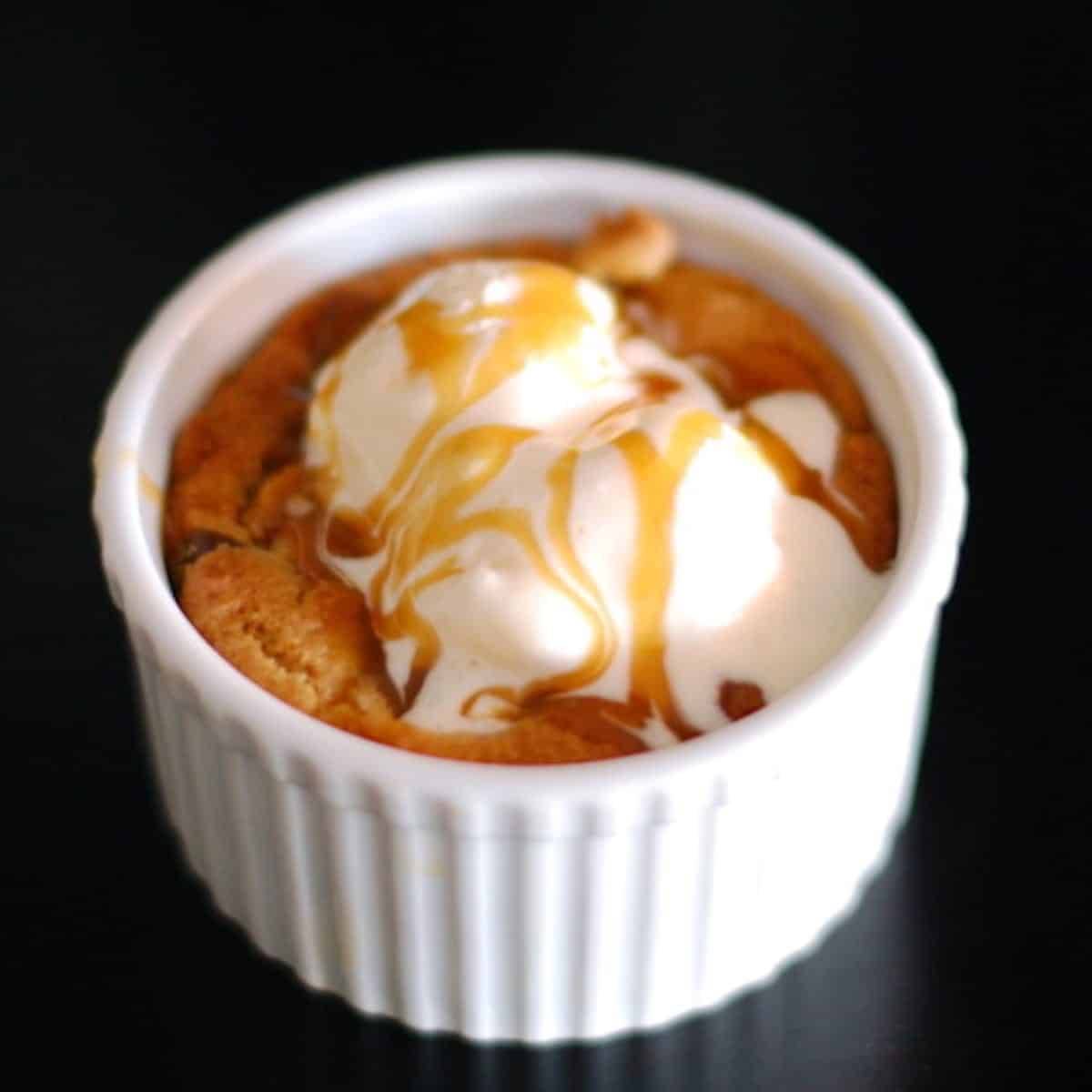 Deep Dish Chocolate Chip Cookie in a white bowl with ice cream and caramel topping.