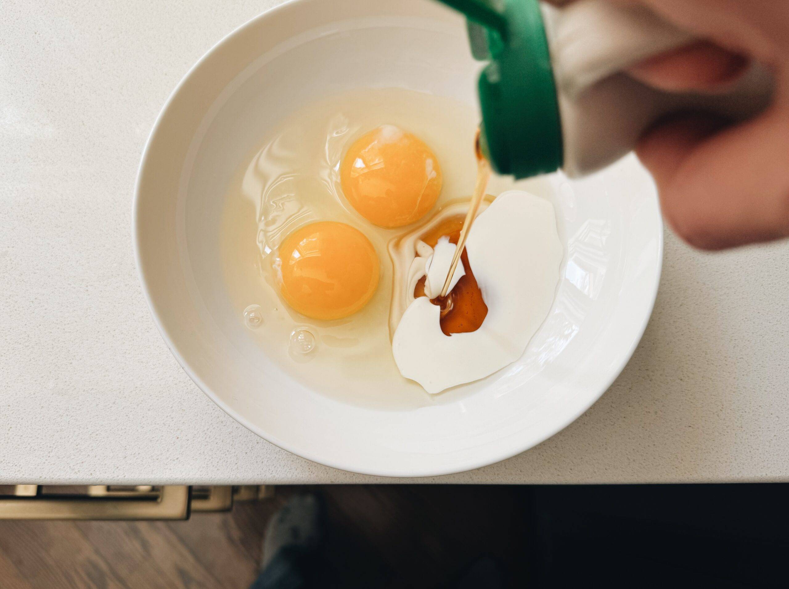 Pouring maple syrup into a bowl with eggs, cream, and vanilla.