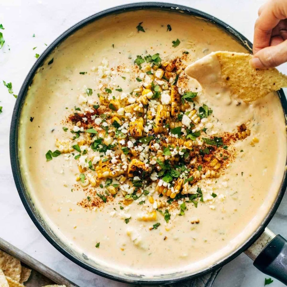 A person dipping a chip into elote queso.