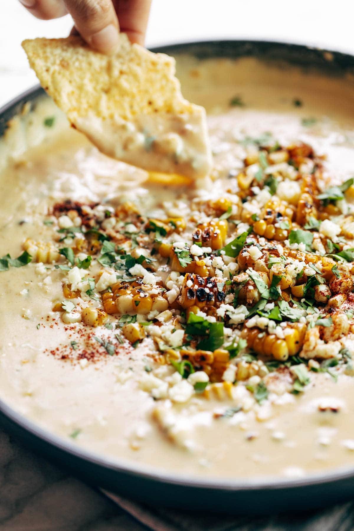 Elote questo in a pan with a chip dipping in.