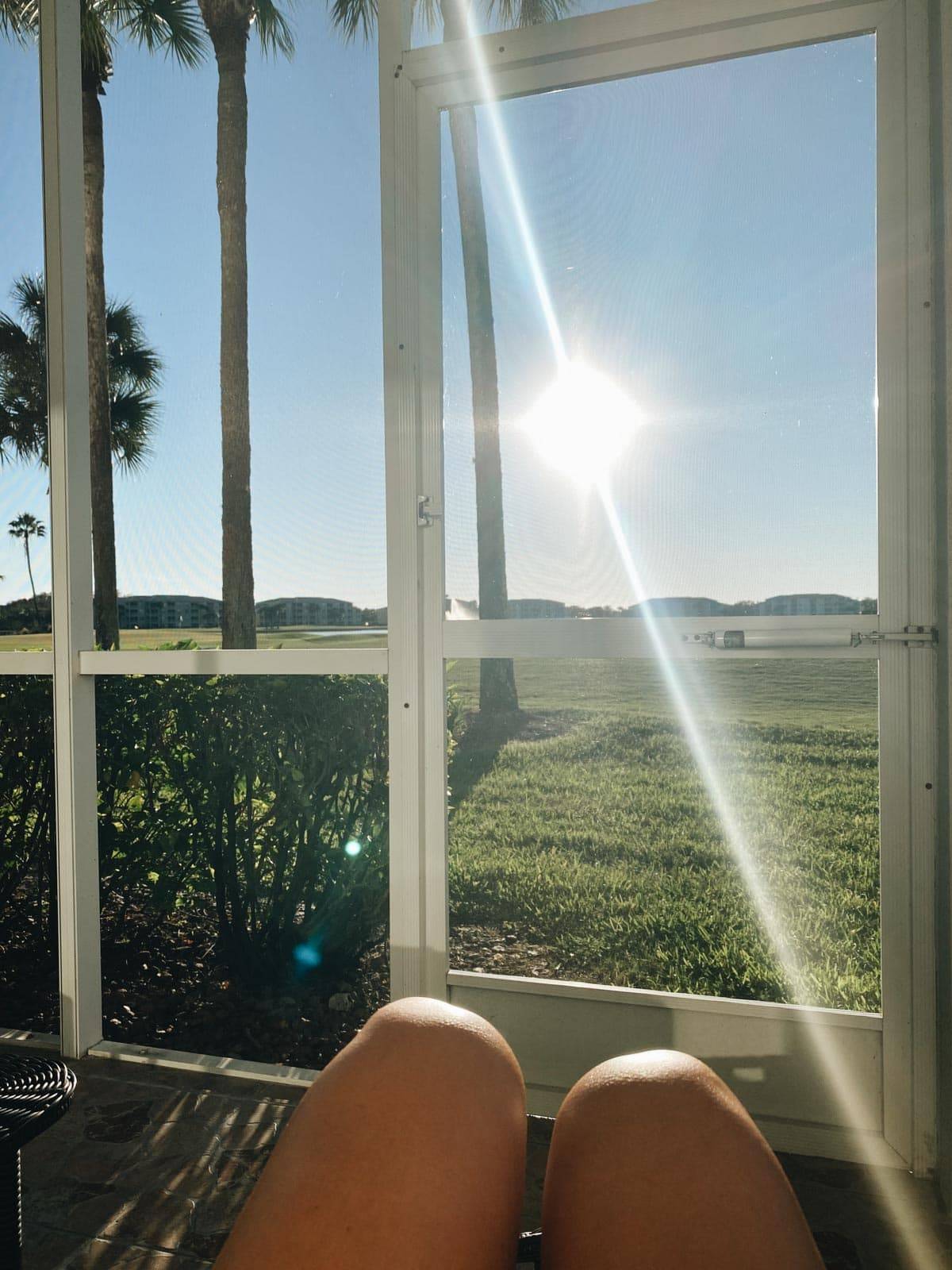A person's knees point towards a sunny yard.
