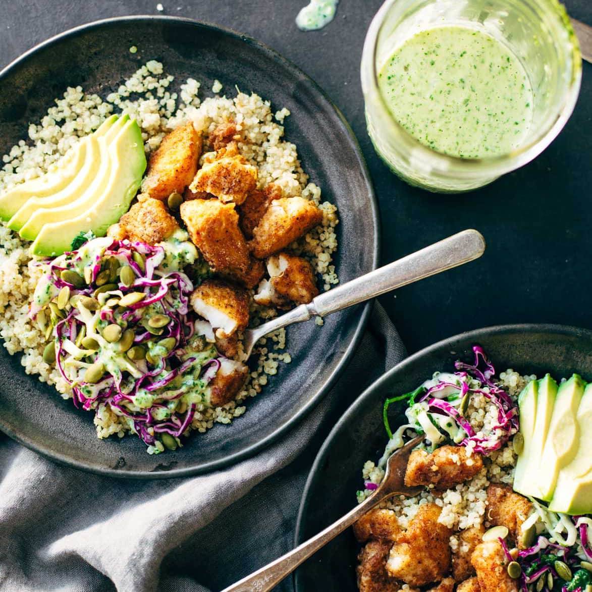 Crispy Spicy Fish Taco Bowls with Cilantro Lime Slaw in two bowls with fresh avocado and two spoons.