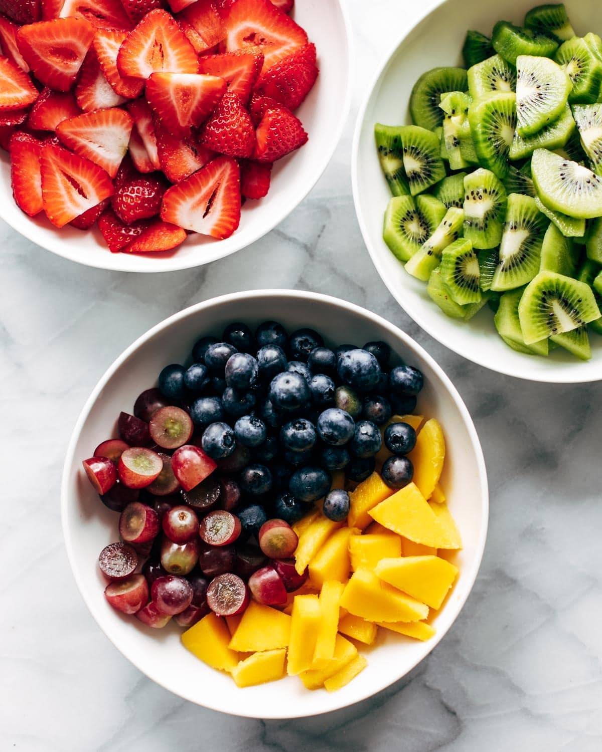 Kiwi, strawberries, blueberries, grapes, and mango in bowls. 