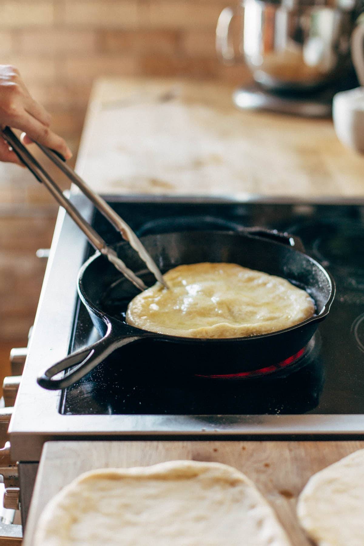 Frying pizza dough in a cast iron pan.