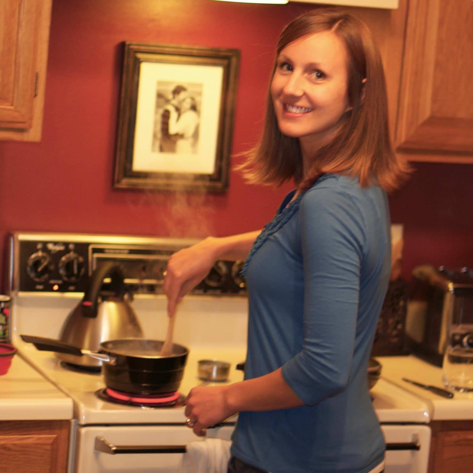 A woman smiling as she stirs food cooking in a pan.