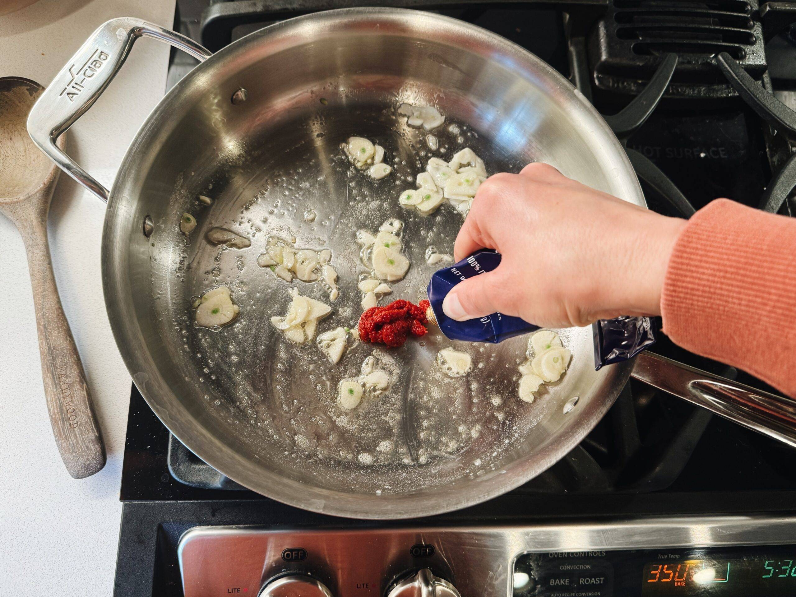 Squeezing tomato paste into a pan with sliced garlic.