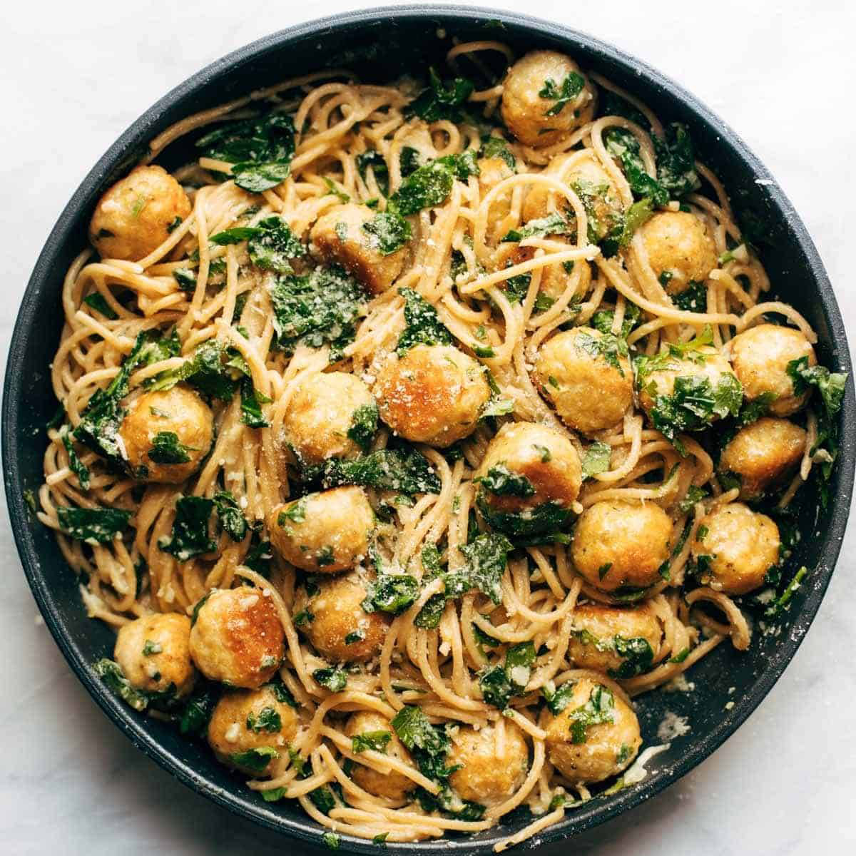 Bowl full of pasta and meatballs sprinkled with cheese, garlic, and herbs.
