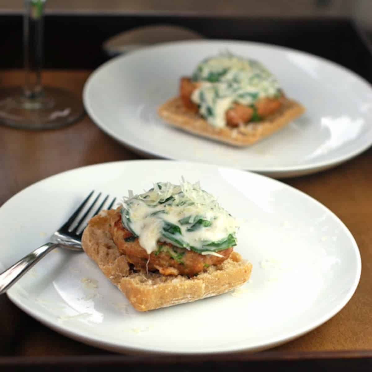 Garlic Parmesan Burgers with Creamed Spinach Sauce on white plates with a fork.