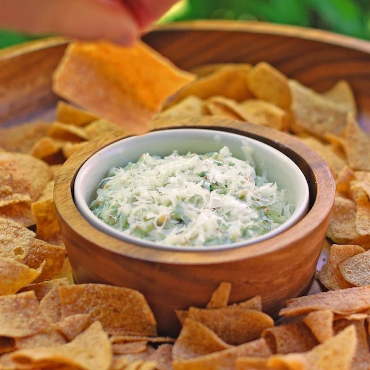 Creamy garlic scape dip with chips in a wooden serving bowl.