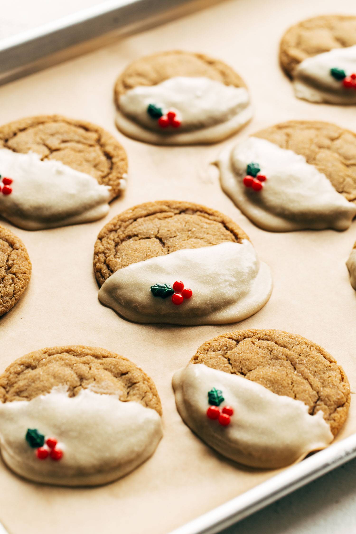 Gingerbread cookies with icing and holly sprinkles on a sheet pan