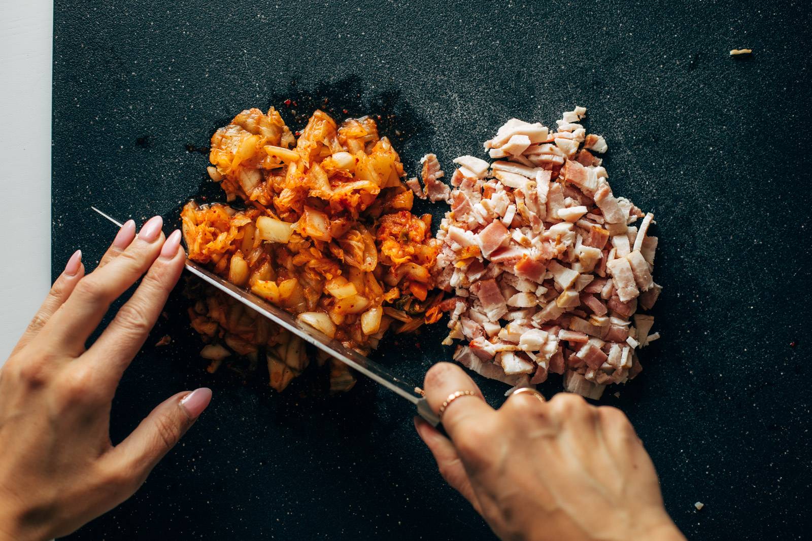 White hand cutting up kimchi and bacon