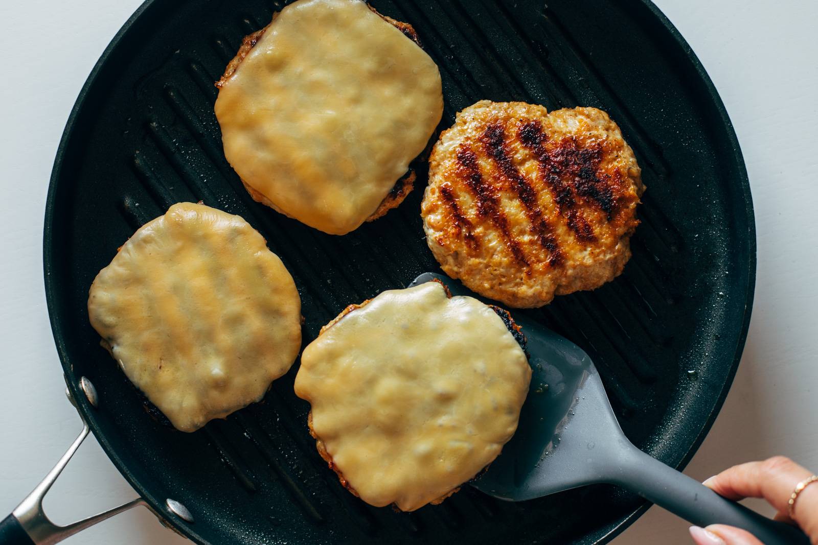 Chicken burgers being fried in a grill pan with a slice of cheese on top