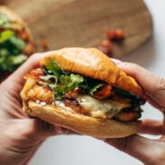 White hands holding chicken burgers with toppings