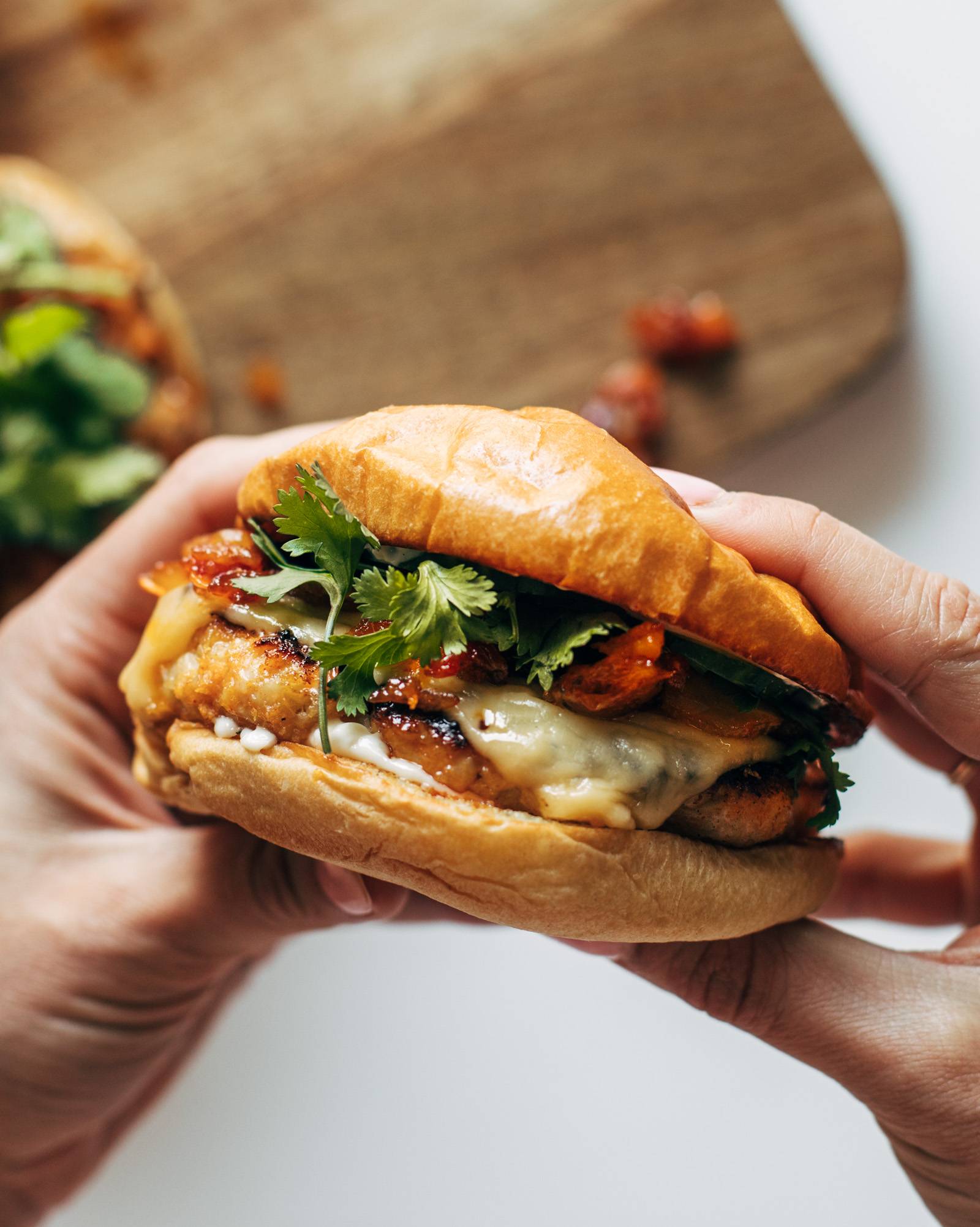 White hands holding chicken burgers with toppings