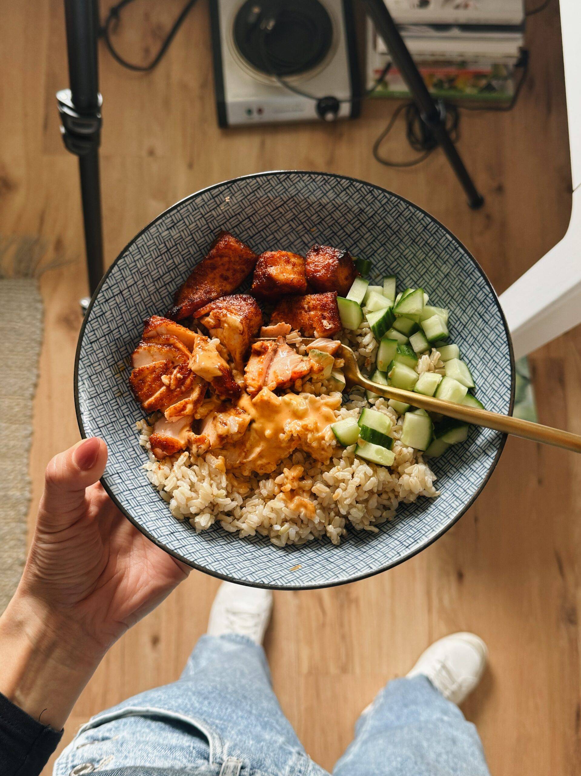 A bowl with rice, salmon, cucumber, and gochujang sauce.