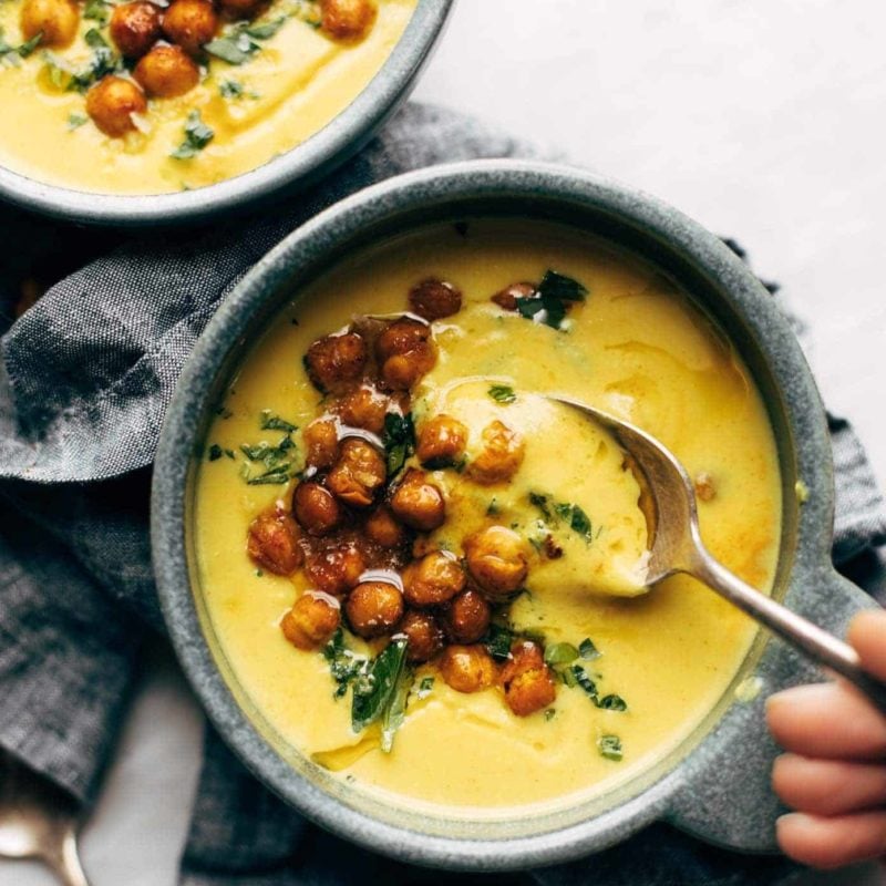 Two bowls of golden soup with roasted chickpeas and olive oil drizzled on top.