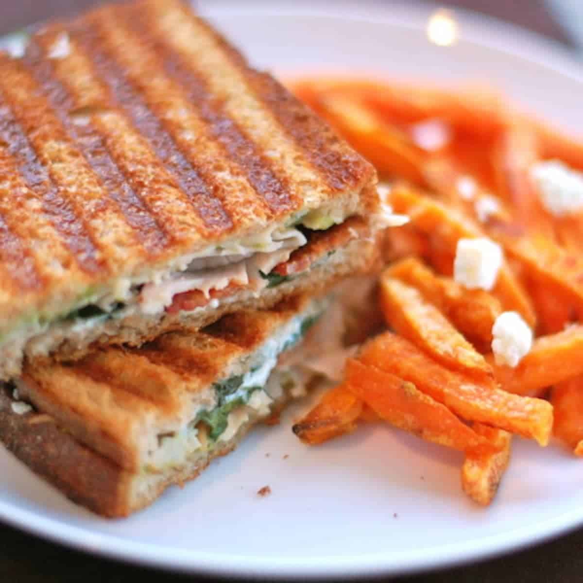 Gorgonzola and bacon panini with spinach on a plate with sweet potato fries.