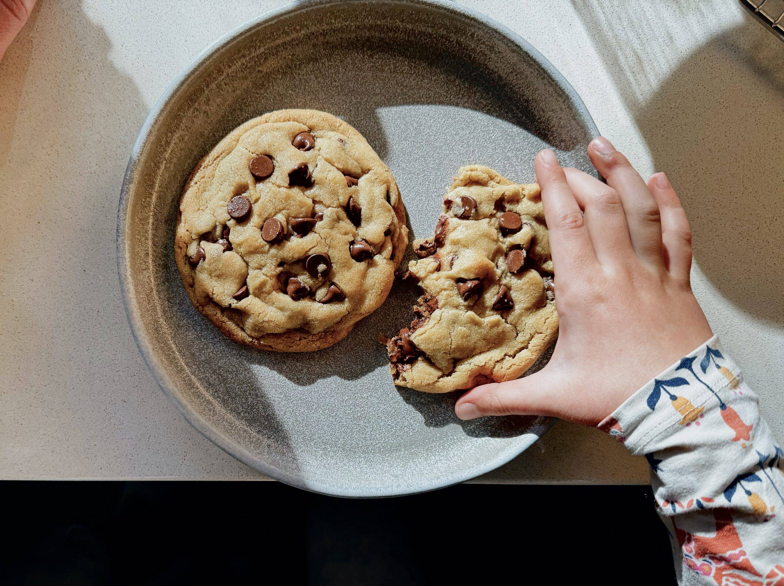 Child's hand reaching for chocolate chip cookie.