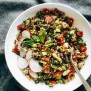 A mixture of quinoa, mint, tomatoes, white beans and radish slices in a bowl.