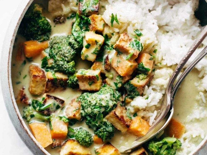 Utensils sit in a bowl of rice, vegetables and tofu.