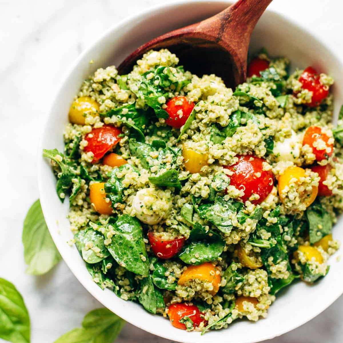 Quinoa and baby spinach tossed with green goddess sauce in a bowl with a wooden spoon.