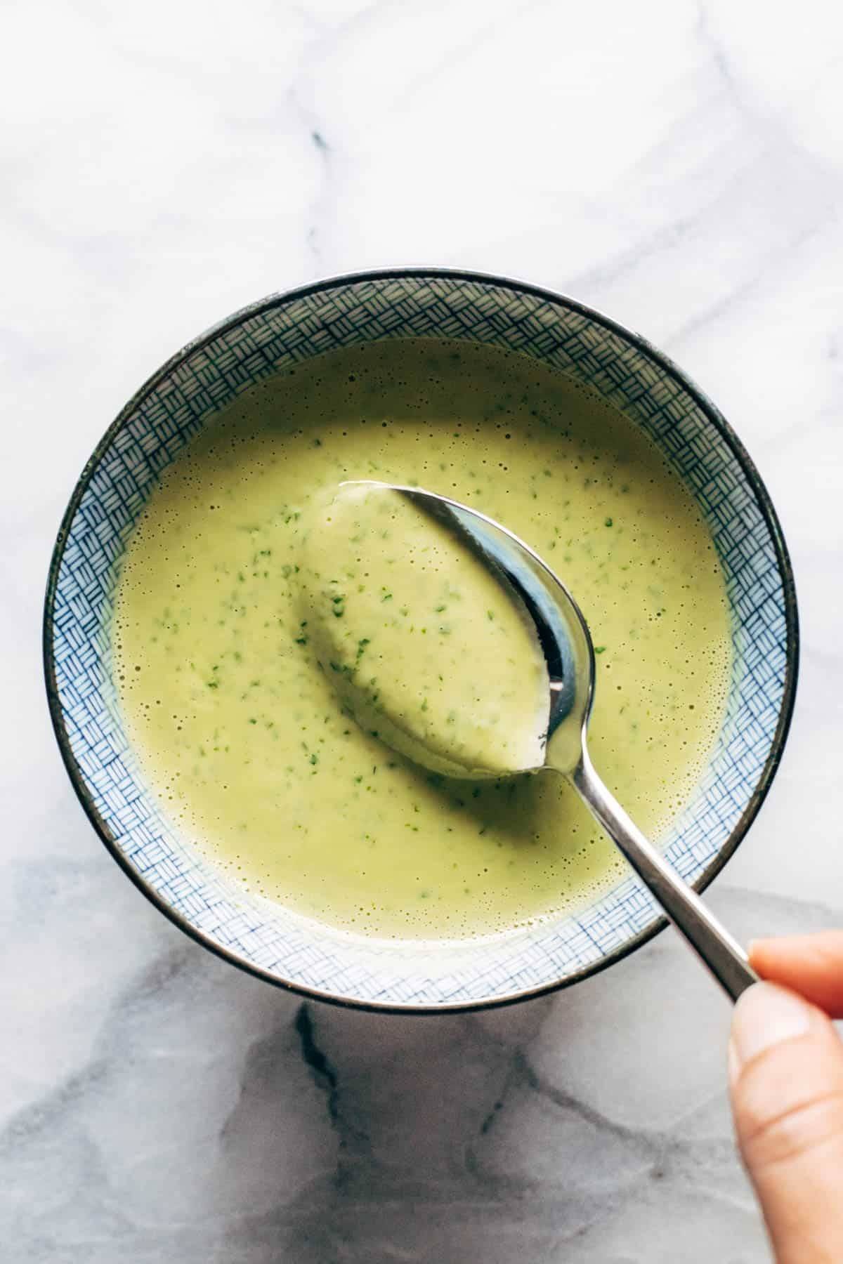 A spoon being dipped into green tahini sauce.