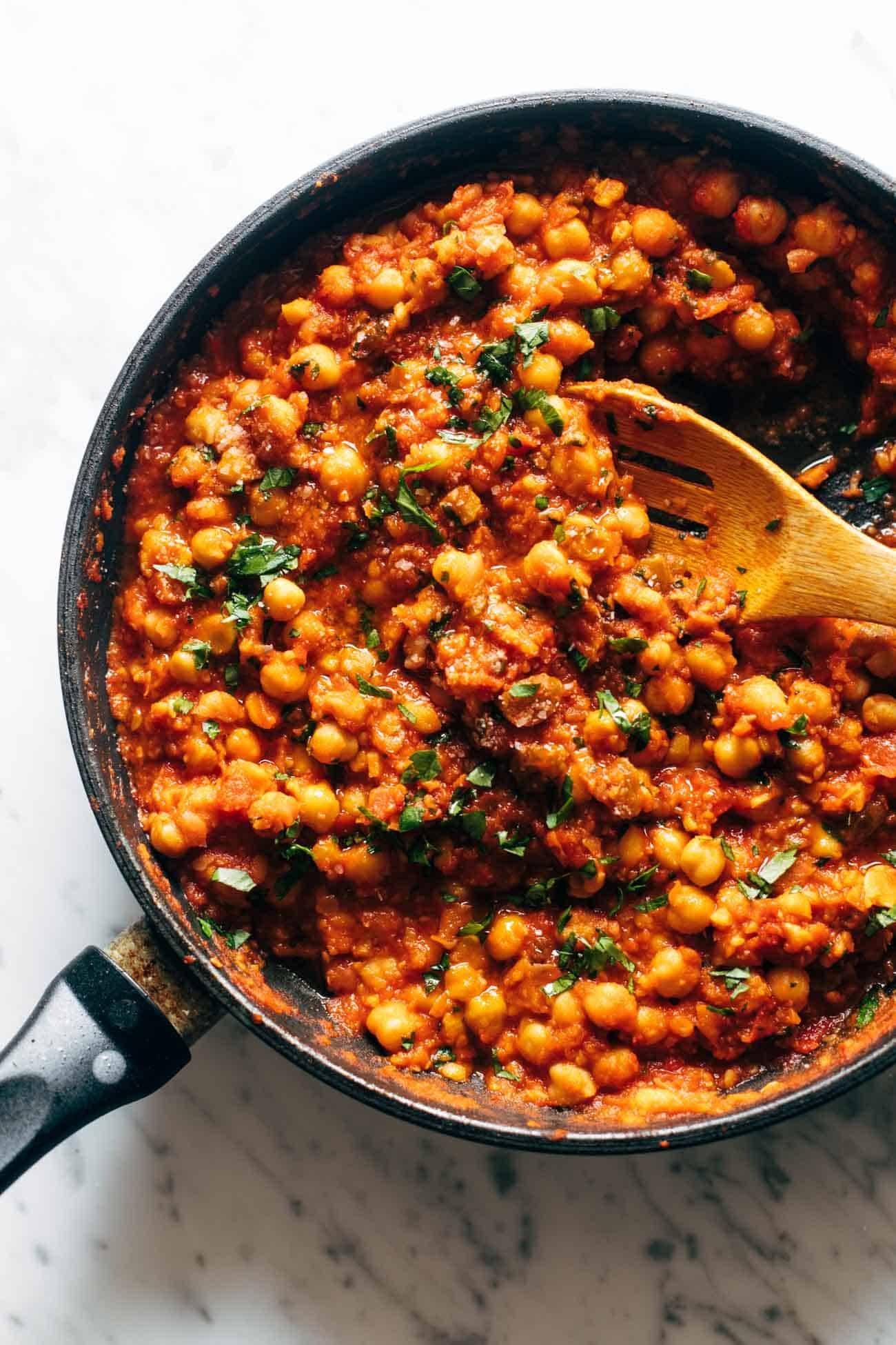 Harissa chickpeas in a pan with a wooden spoon and parsley sprinkled on top. 