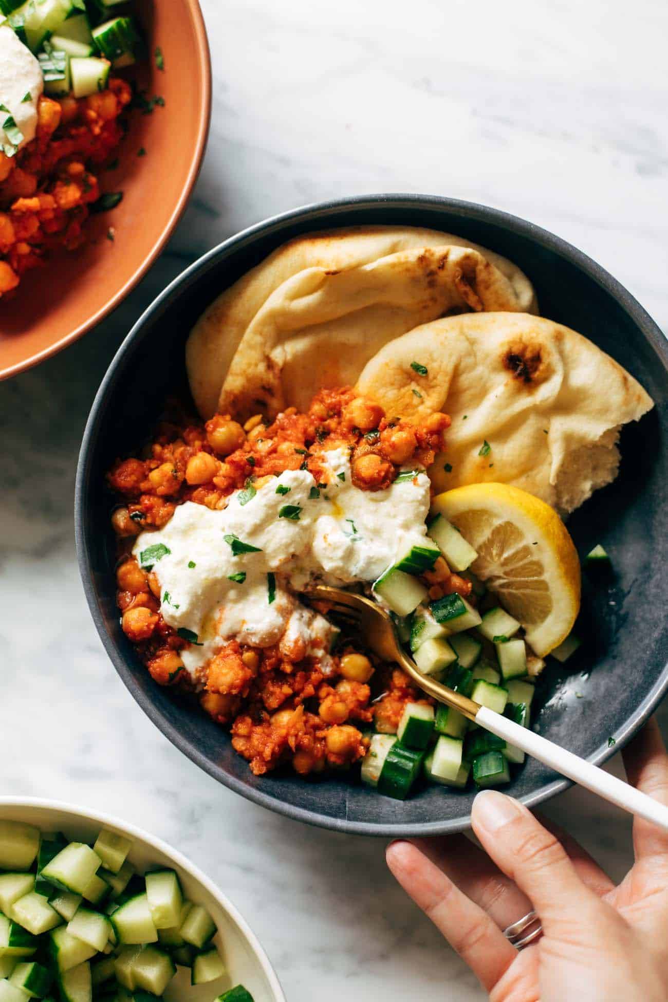 Harissa chickpeas with whipped feta in a bowl with cucumbers, lemon, and naan. 