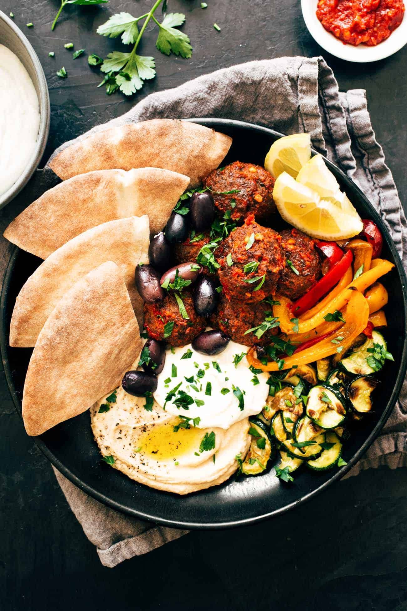 Harissa Meatballs with Whipped Feta in a bowl with peppers, zucchini, and pita bread