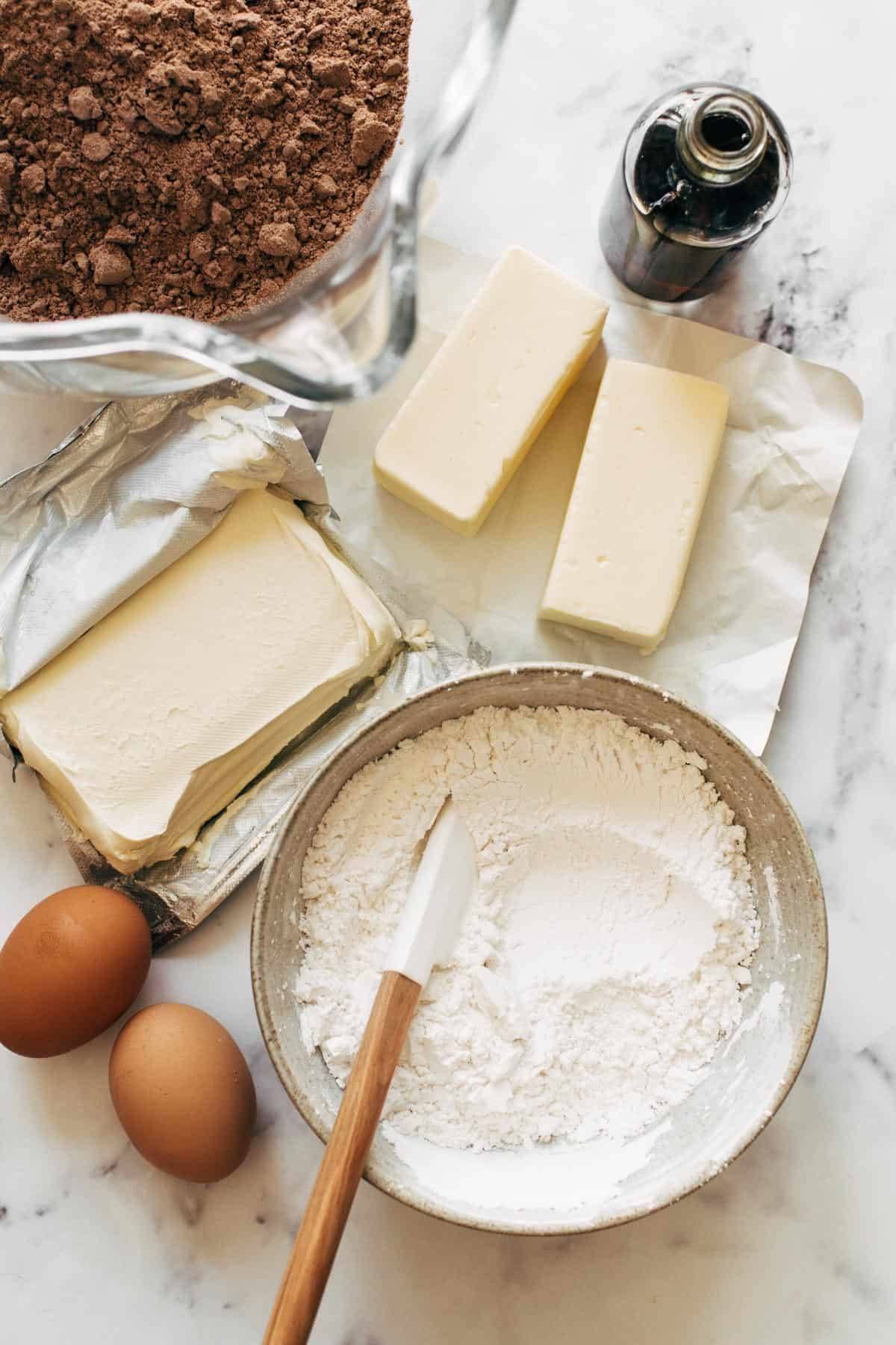 Cocoa powder, vanilla, butter, cream cheese, flour, and eggs on a counter top.