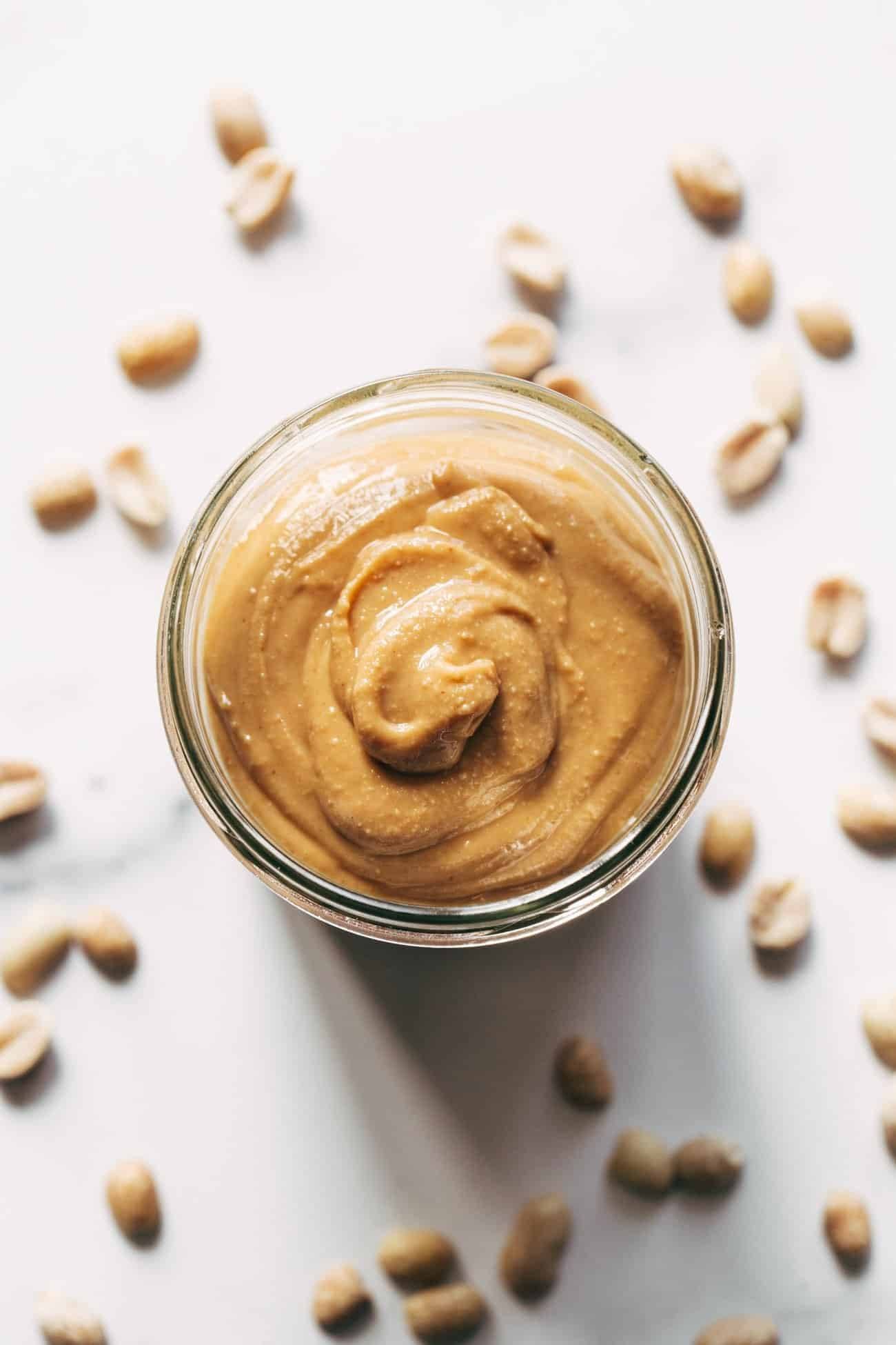 Homemade peanut butter in a jar surrounded with peanuts