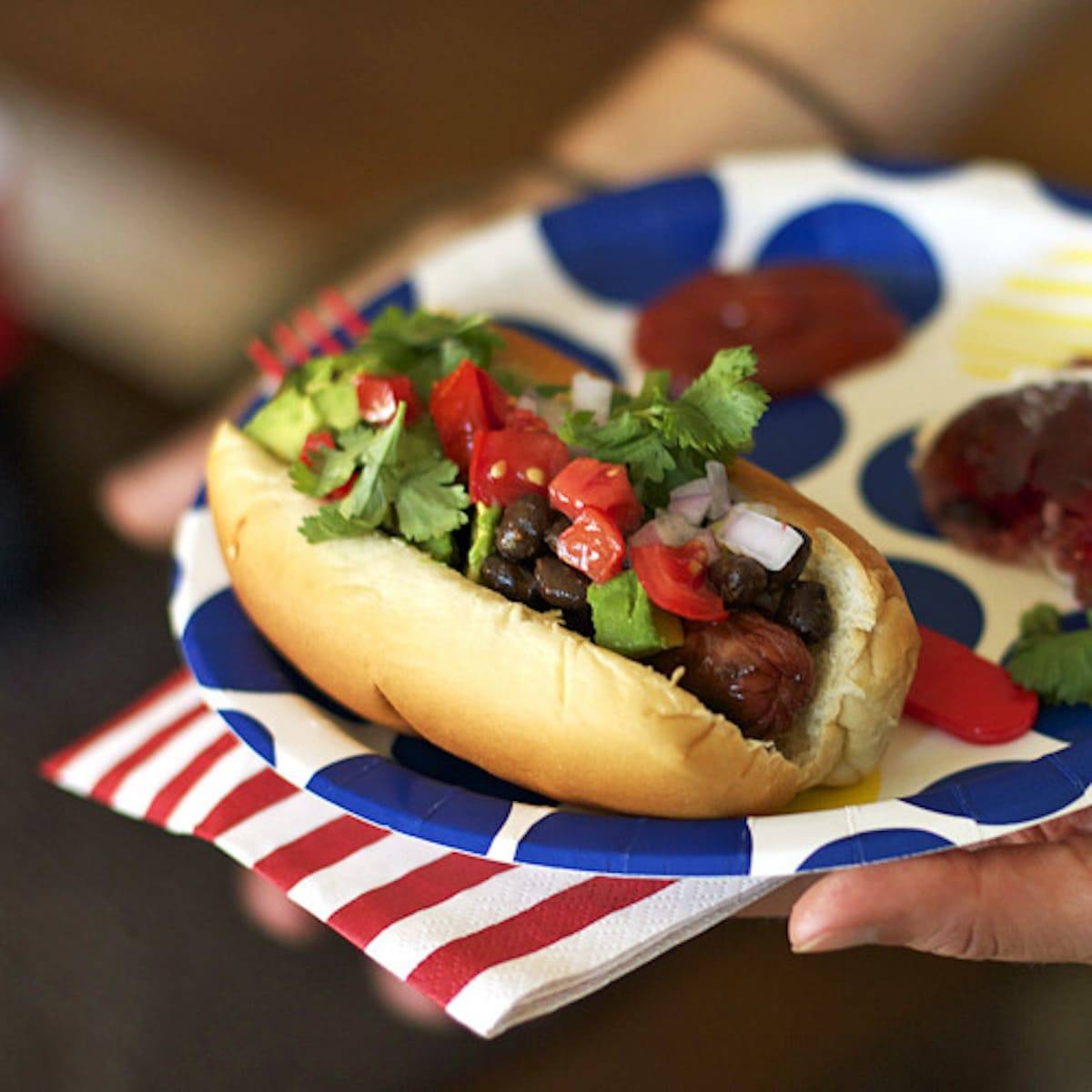 Hot dog with toppings on a red, white, and blue plate.