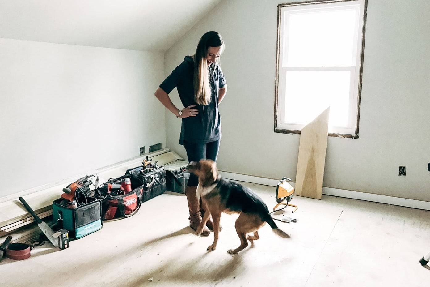 A woman laughing as she looks at her dog in a house that is being remodelled.