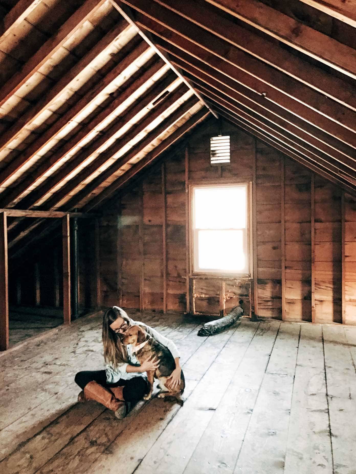 A girl sitting on the wooden floor with her dog in an empty wooden attic.