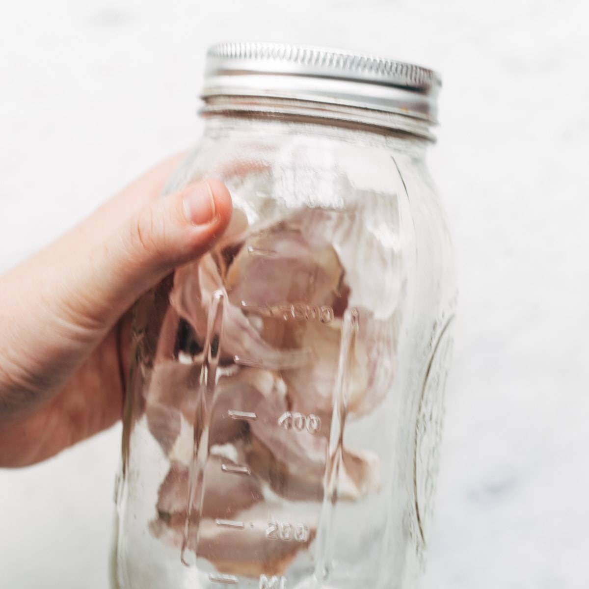 A hand holds a jar of garlic cloves.