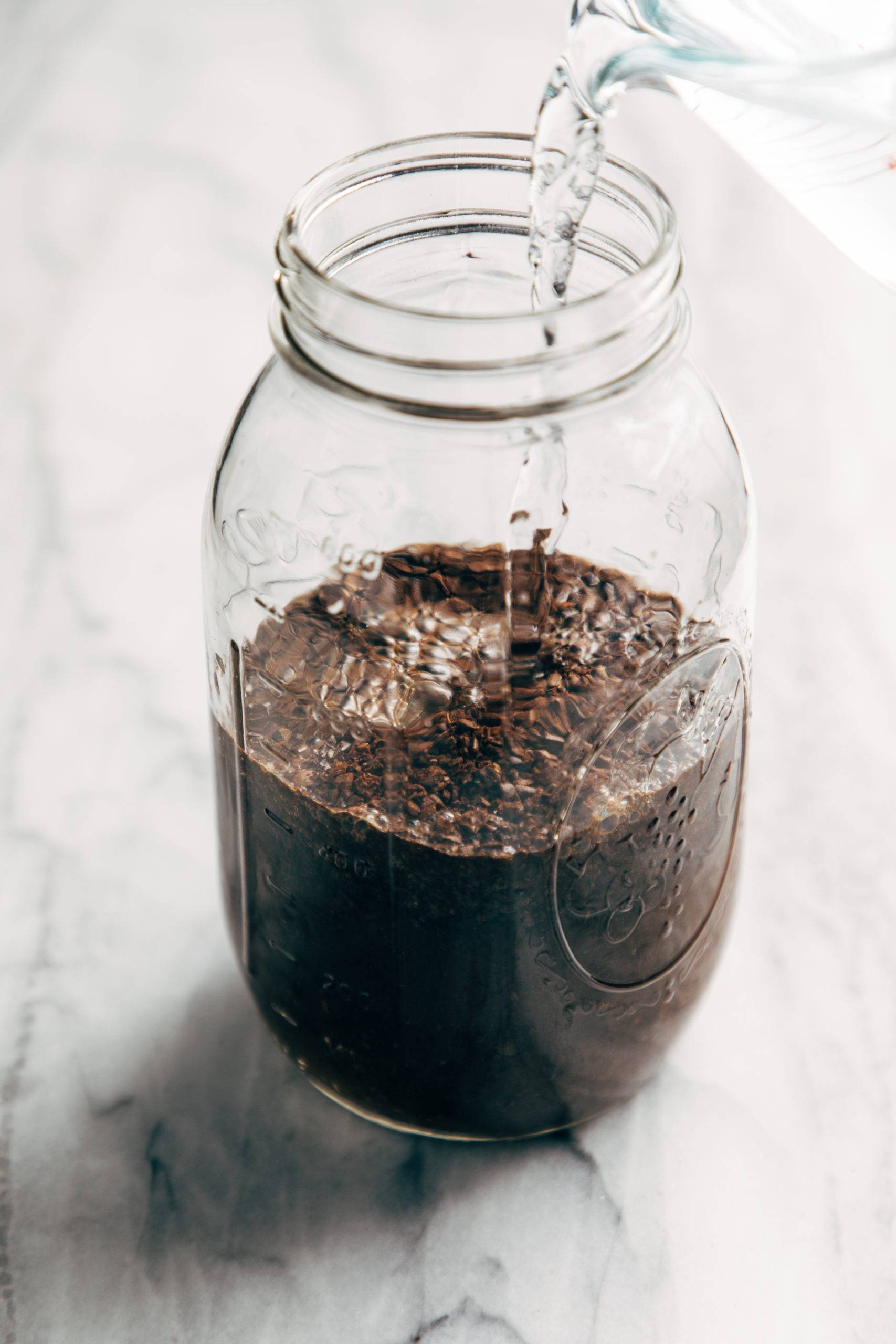 Water being poured over coffee grounds in a mason jar for cold brew coffee
