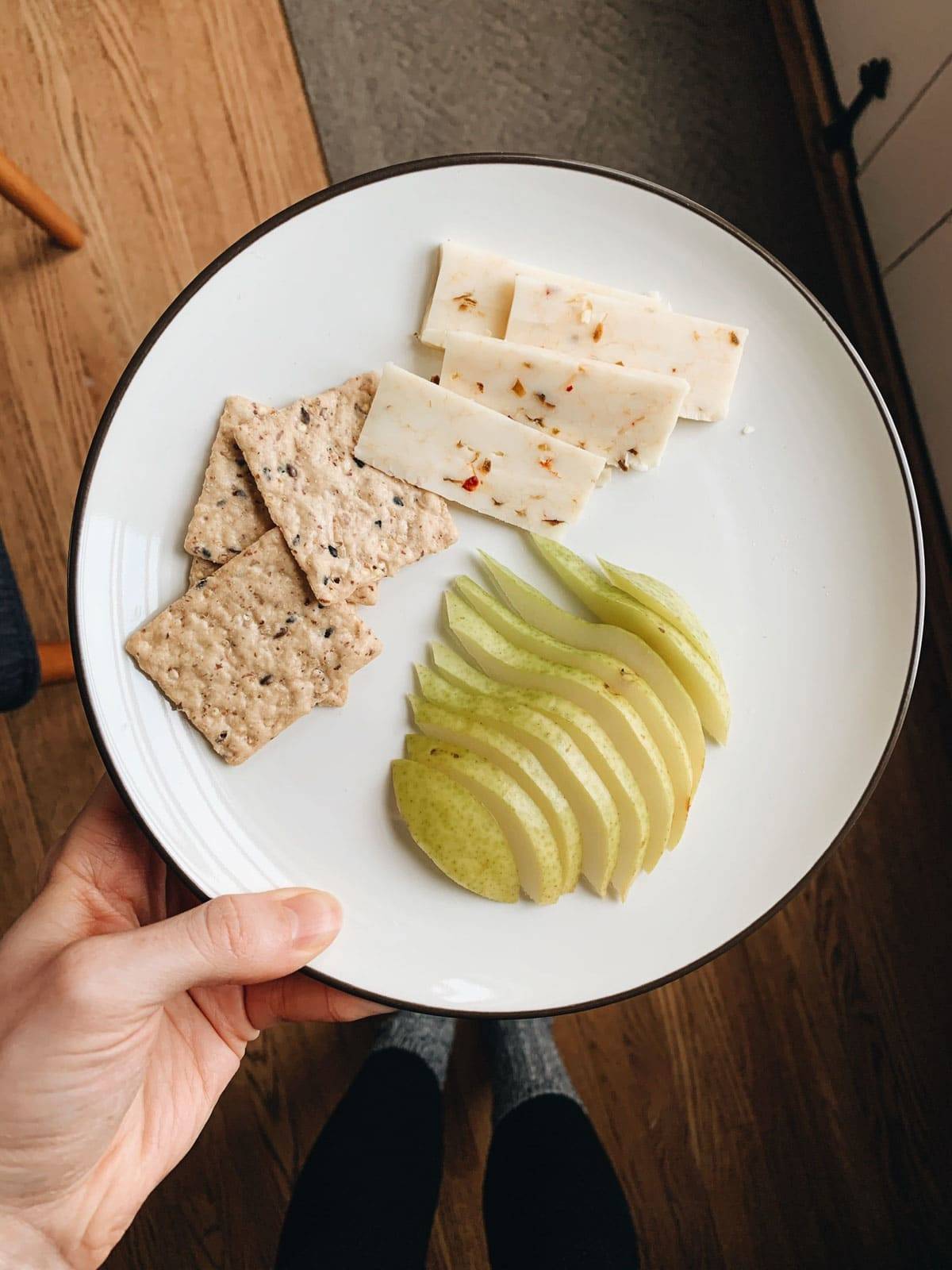 Crackers, cheese and fruit on a plate.