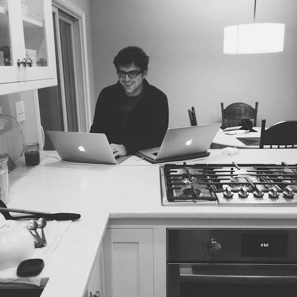 Man on two computers in a kitchen.