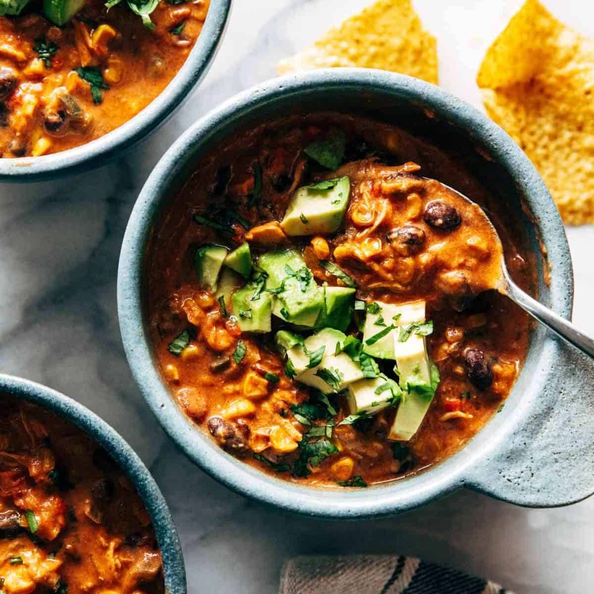 Queso chicken chili topped with avocado in a grey bowl.