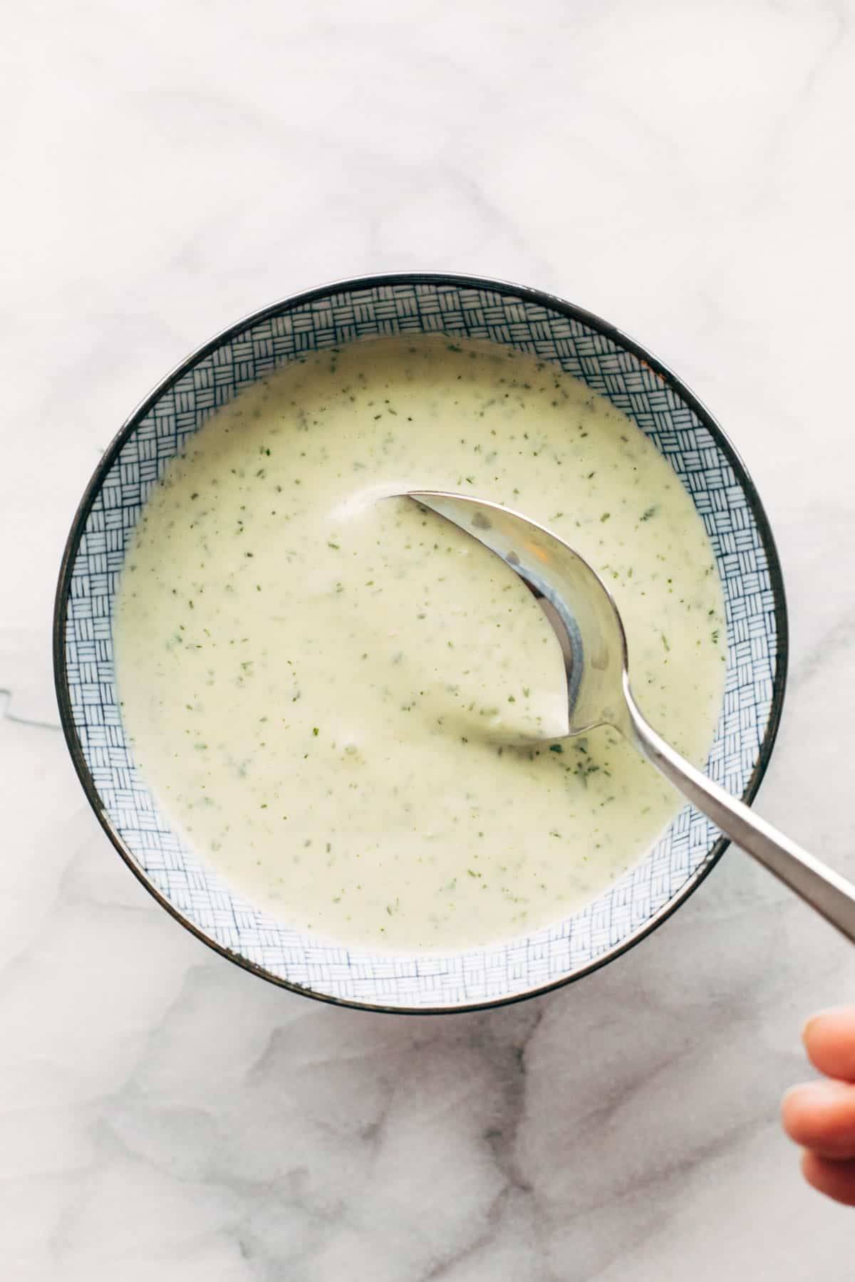 A spoon stirring a jalapeno ranch in a bowl.