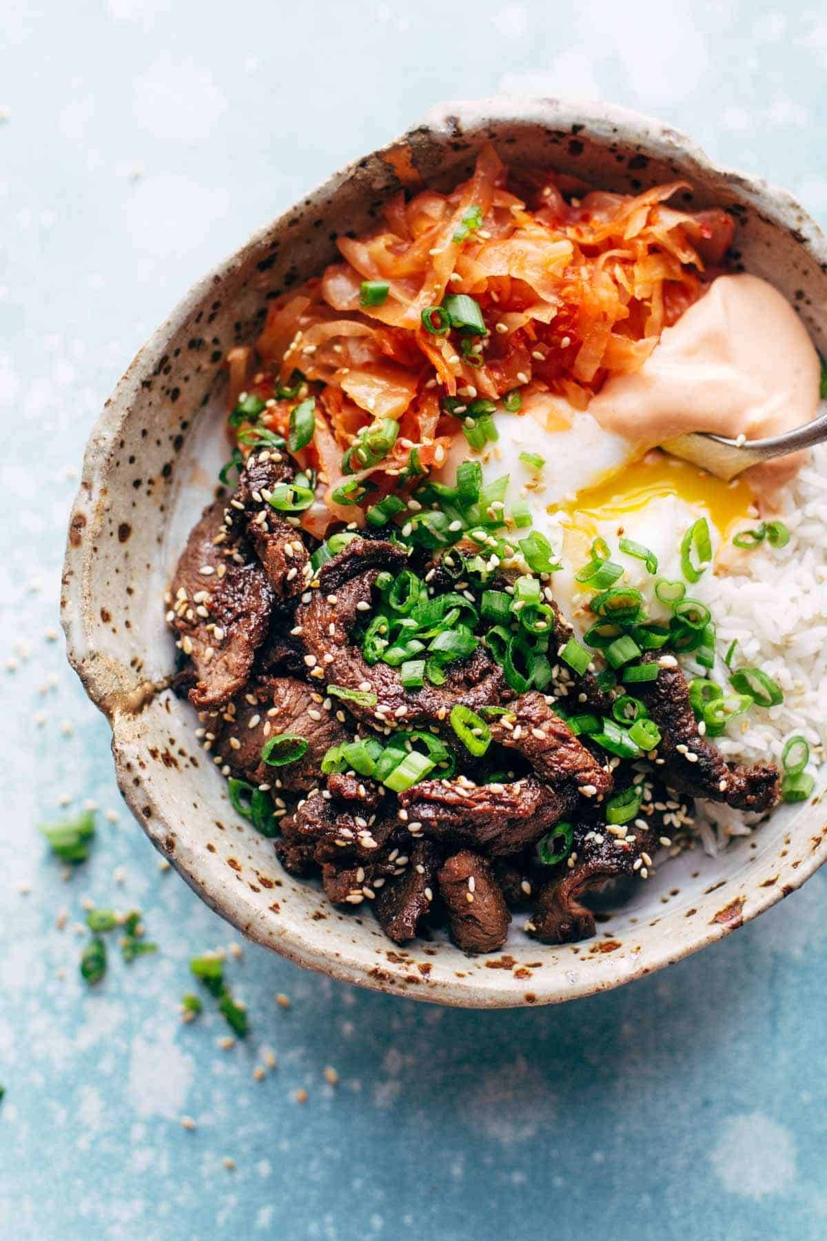 Korean beef along with carrot, onion and spicy mayo in a bowl with a spoon.