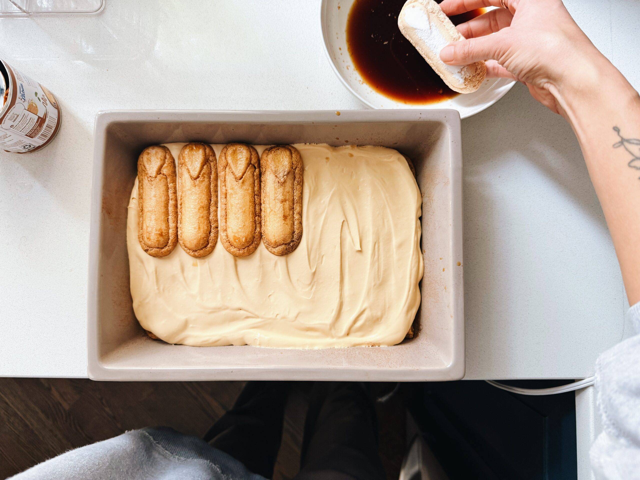 Soaking ladyfingers in espresso and layering in a pan.