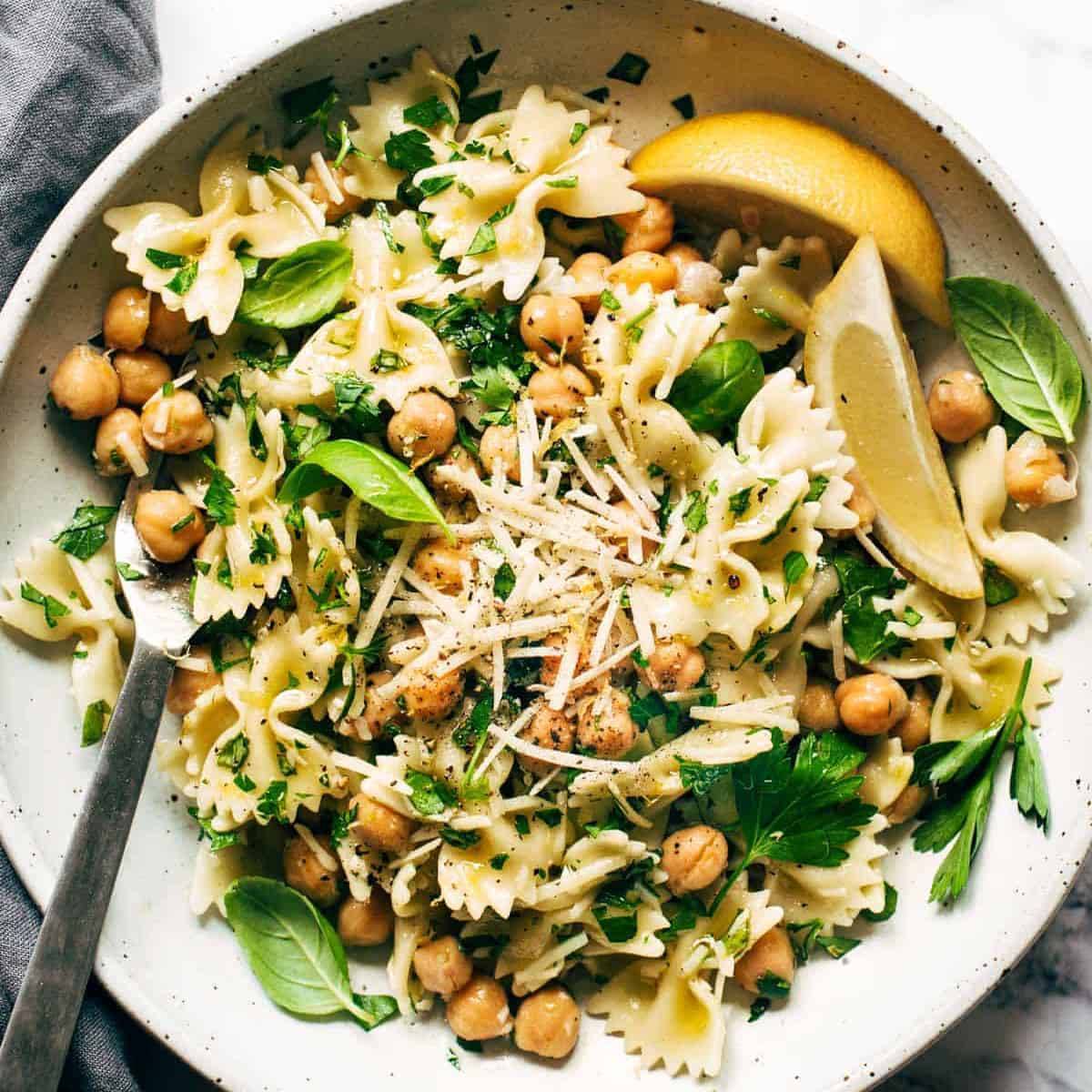 Pasta tossed with greens and cheese with lemon wedges.