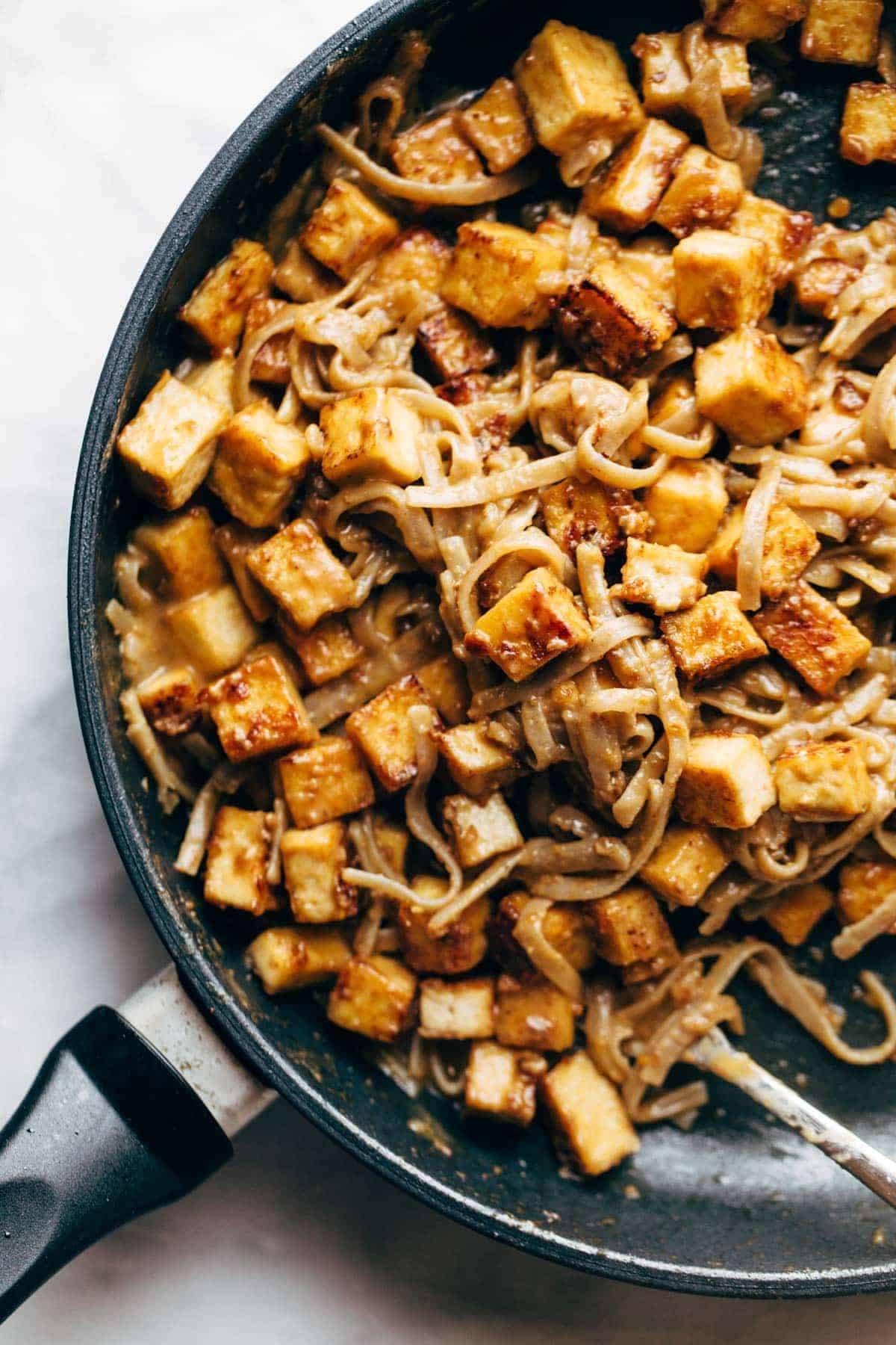 Fried tofu and brown rice noodles with sauce in pan.