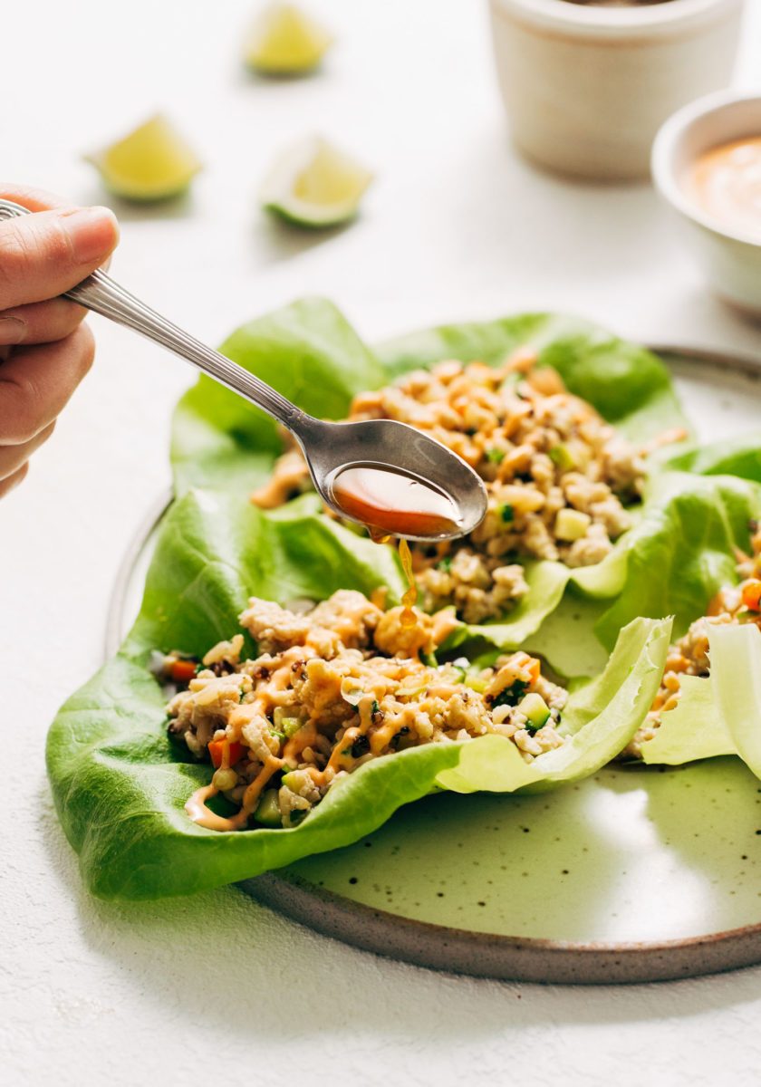 Chicken lettuce cups on plate with hand and fork going in for a bite.