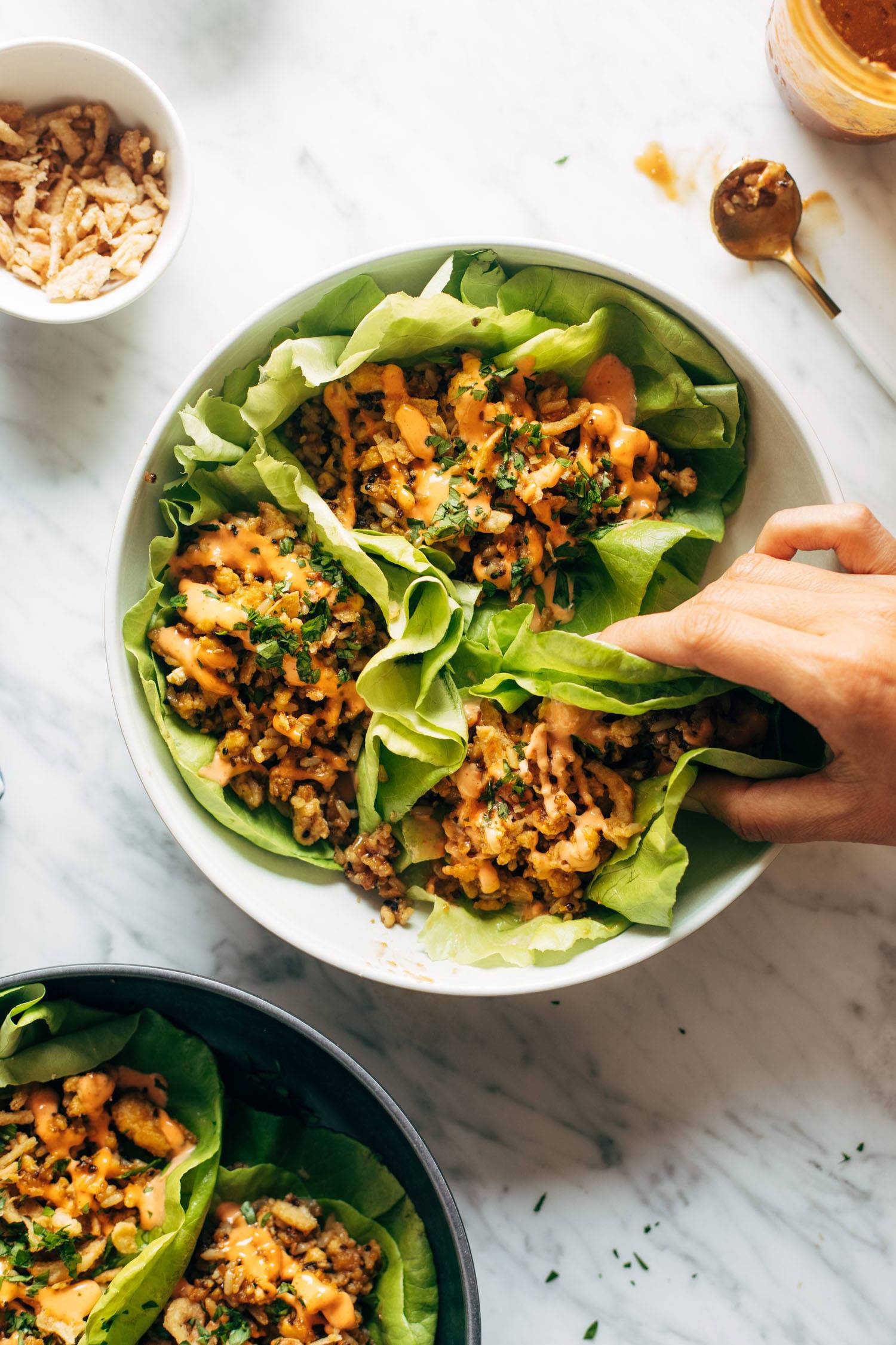 White hand grabbing a brown rice tofu lettuce wrap with peanut sauce drizzled on top. 