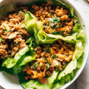 Lettuce wraps on a plate. The wraps are filled with tofu and brown rice and have sauce drizzled on top.