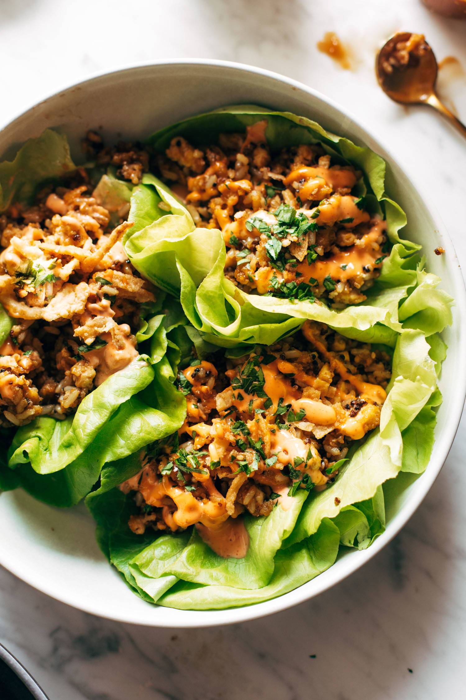 Lettuce wraps on a plate. The wraps are filled with tofu and brown rice and have sauce drizzled on top.