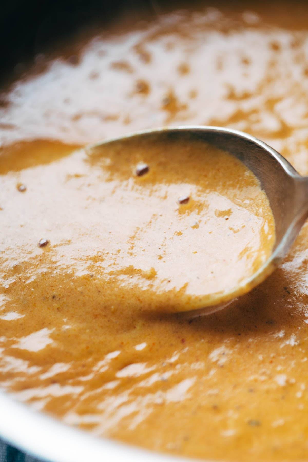 Masala sauce simmering in a pan with a spoon.