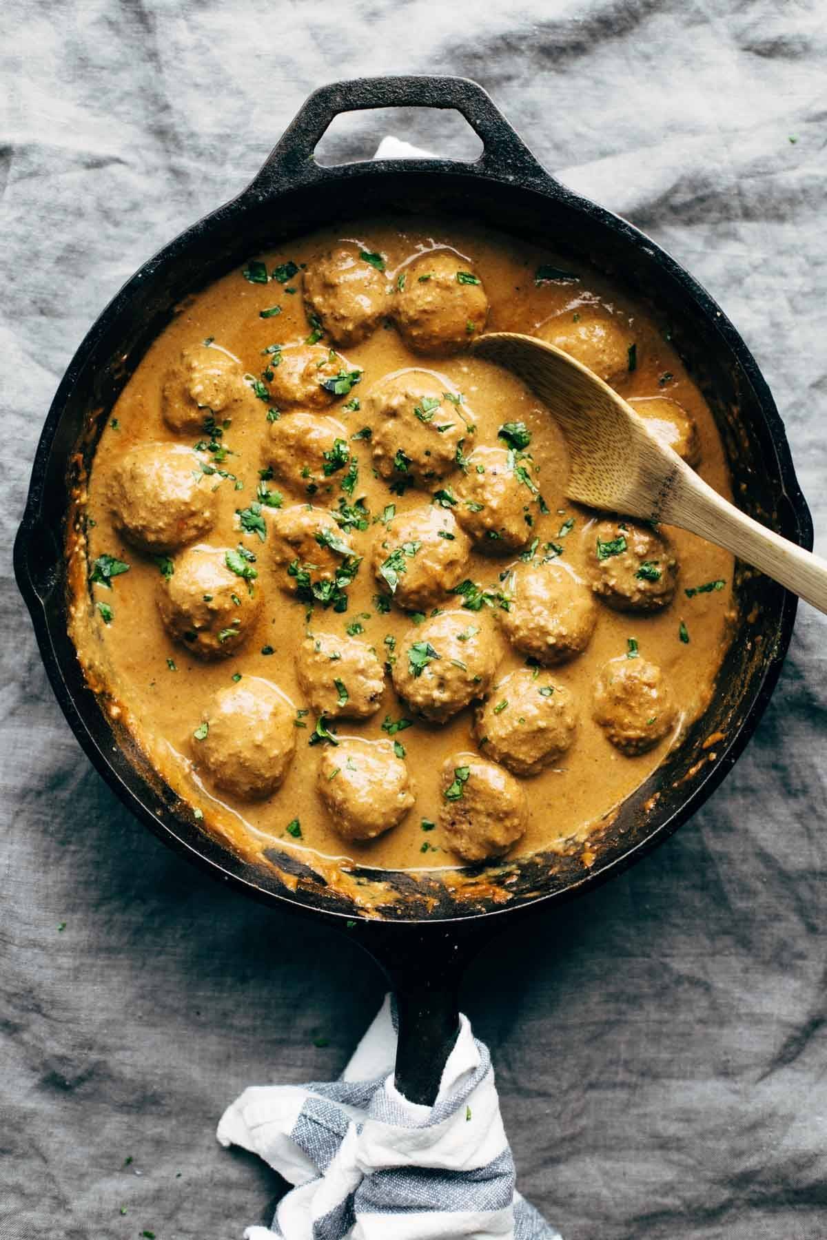 Masala sauce on meatballs in a skillet with a wooden spoon and a napkin.